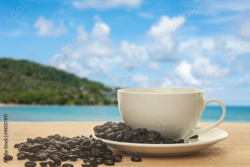 Cup of coffee with coffee bean on the beach background