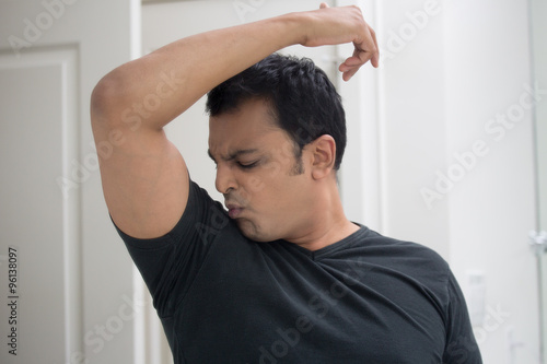 Obraz na plátne Closeup portrait, grumpy sweaty young man in black t-shirt, sniffing himself, very foul situation, isolated mirror reflection