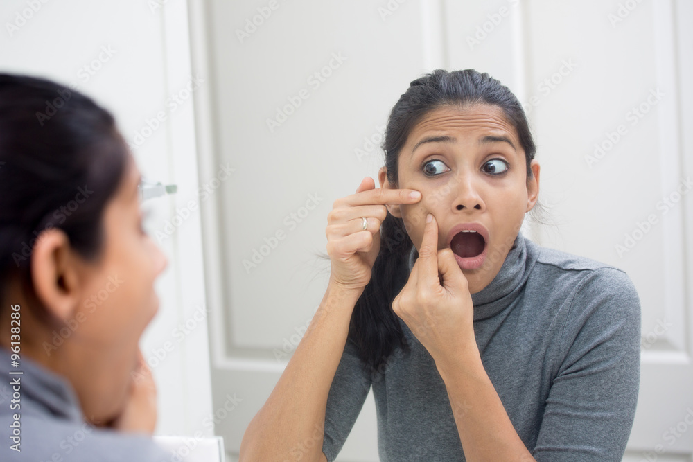 Closeup portrait of young frustrated woman surprised stunned to see zit on her face, gray turtleneck, isolated mirror reflection background. Facial feelings, situation, reaction Closeup portrait of young frustrated woman surprised stunned to see zit on her face, gray turtleneck, isolated mirror reflection background. Facial feelings, situation, reaction
