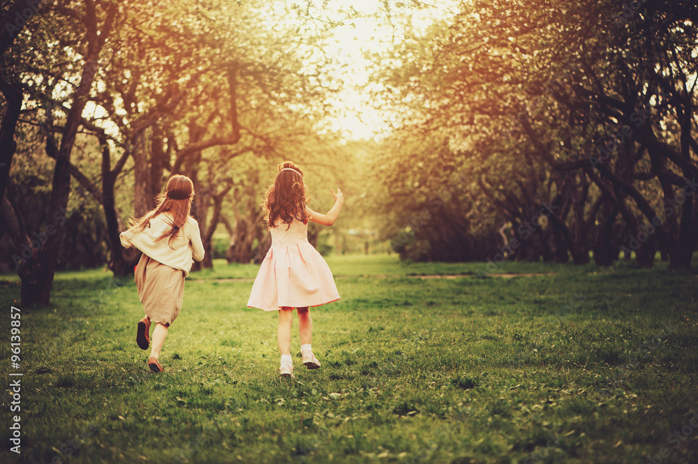 Obraz premium two happy dressy girls running on spring walk, outdoor activities, friendship concept