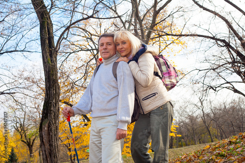  Mature man and woman hikers stand embracing in autumn forest 
