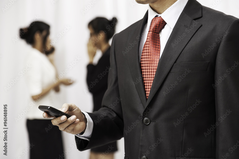 businessman using his mobile phone while two women are talking in the background
businessman using his mobile phone while two women are talking in the background