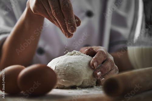 Female in chef uniform adding flour to dough preparing pizza in the kitchen. Cookery and healthy nourishment concept. 
