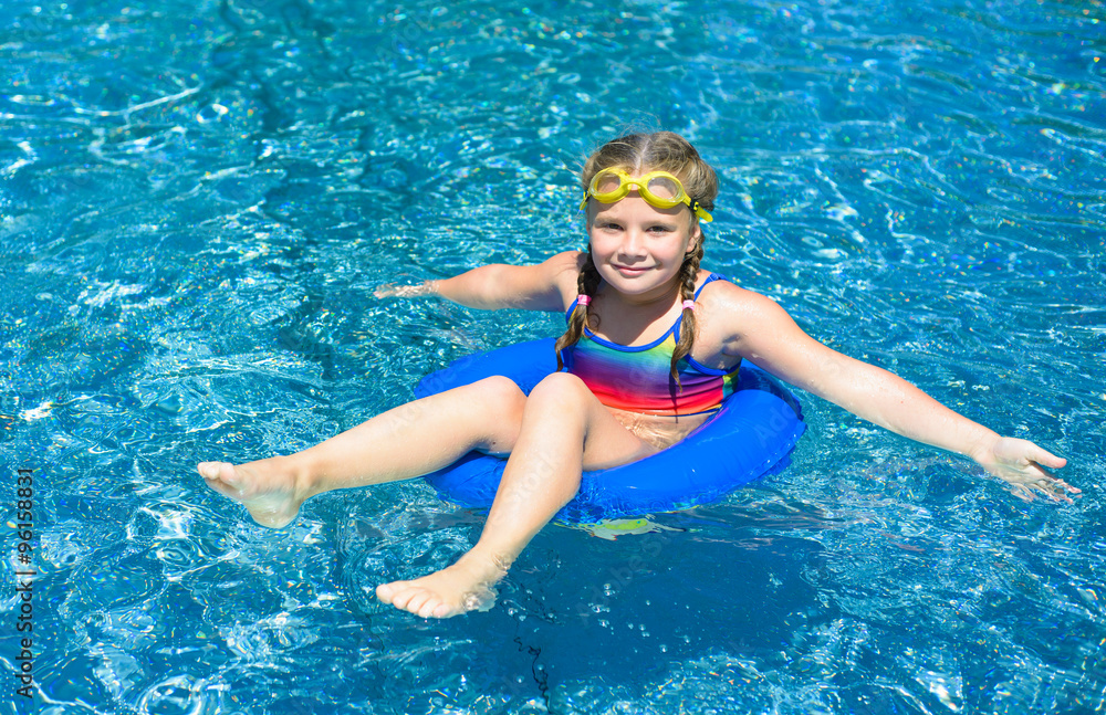 Smiling little girl  with blue life ring has fun in the swimming pool