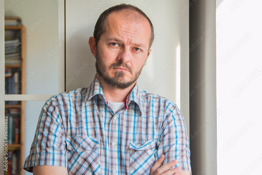 Fototapeta premium Man with beard in plaid shirt standing next to window, posing and looking to camera