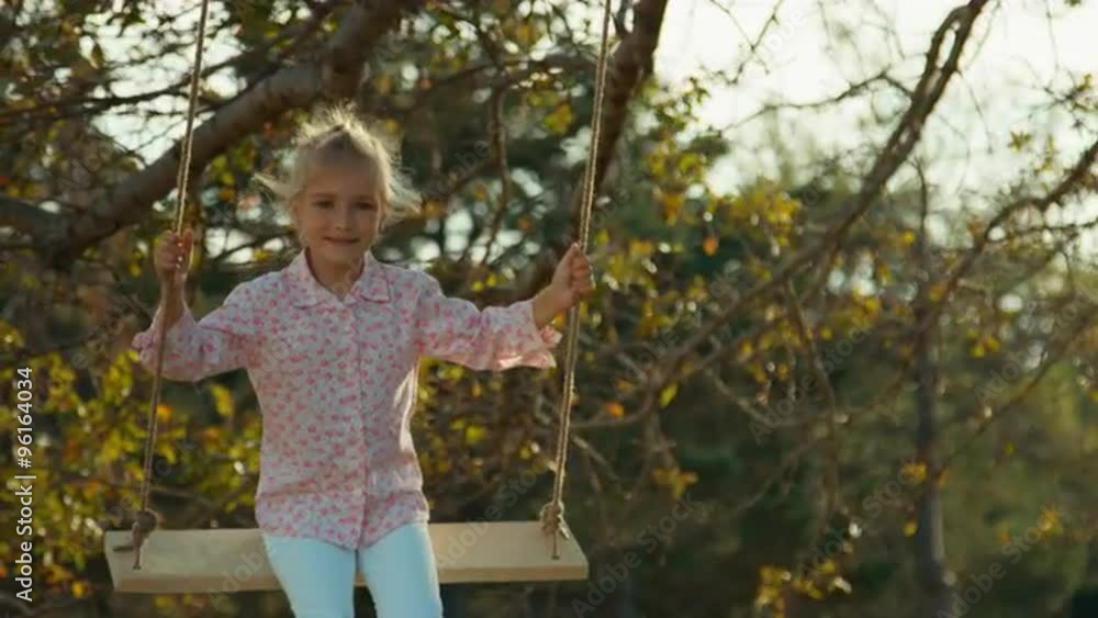 Happy child on a swing under a tree. Girl looking at camera and smiling Happy child on a swing under a tree. Girl looking at camera and smiling