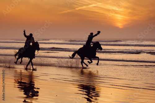 Obraz na plátně Silhouette of a horse and rider galloping on beach at sunset.