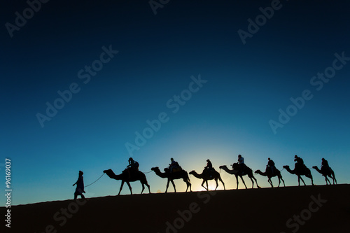 Sillhouette of camel caravan going through the desert at sunset.