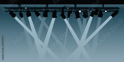 A background silhouette illustration of a spotlight rig shining beams down into the darkness.
