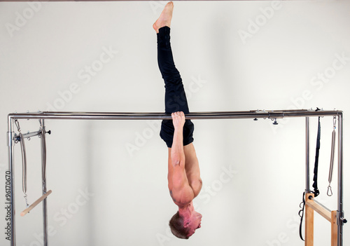 Pilates aerobic instructor man in cadillac fitness exercise acrobatic upside down balance