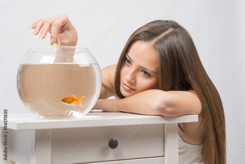 Young girl put her head on his hand, the other hand feeds the fish in the aquarium Young girl put her head on his hand, the other hand feeds the fish in the aquarium