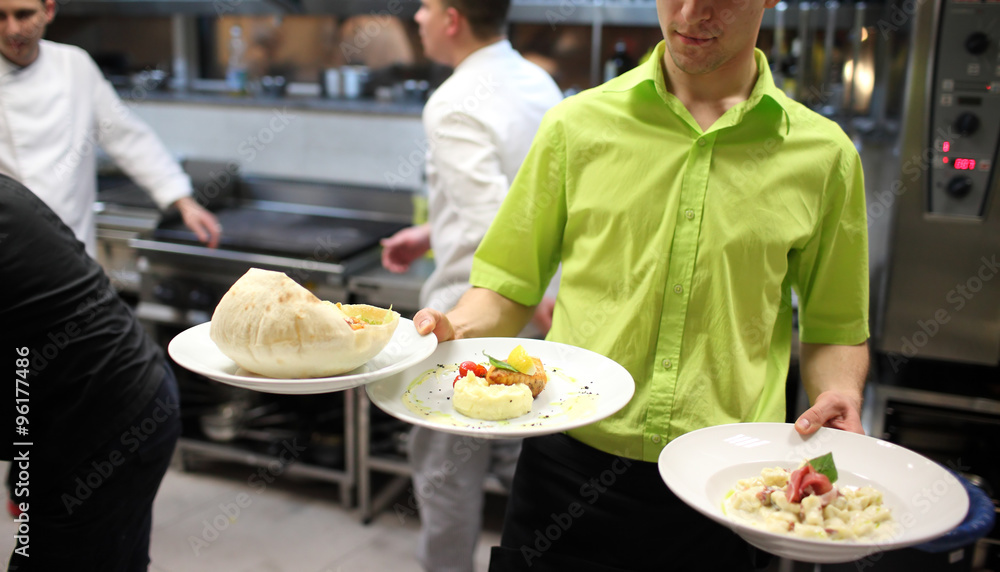 Waiter carrying a plate with salad dish . Cook in the background Waiter carrying a plate with salad dish . Cook in the background