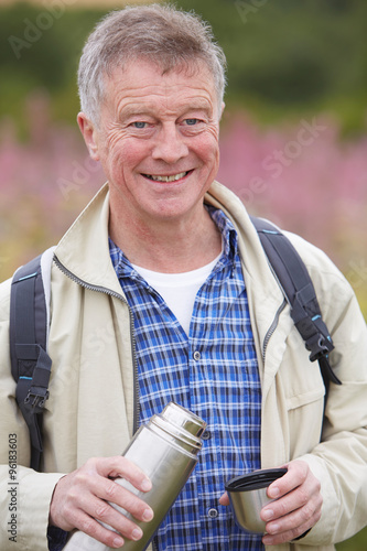 Senior Man Pouring Hot Drink From Flask On Walk