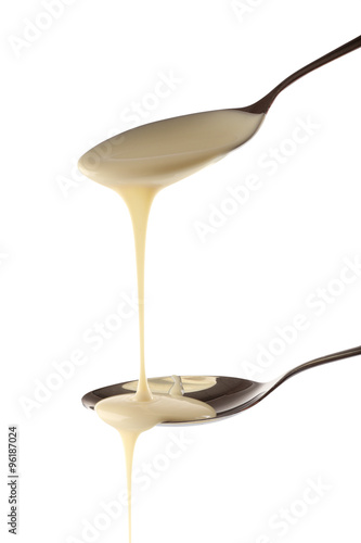 Condensed milk pouring from spoons, isolated on white
