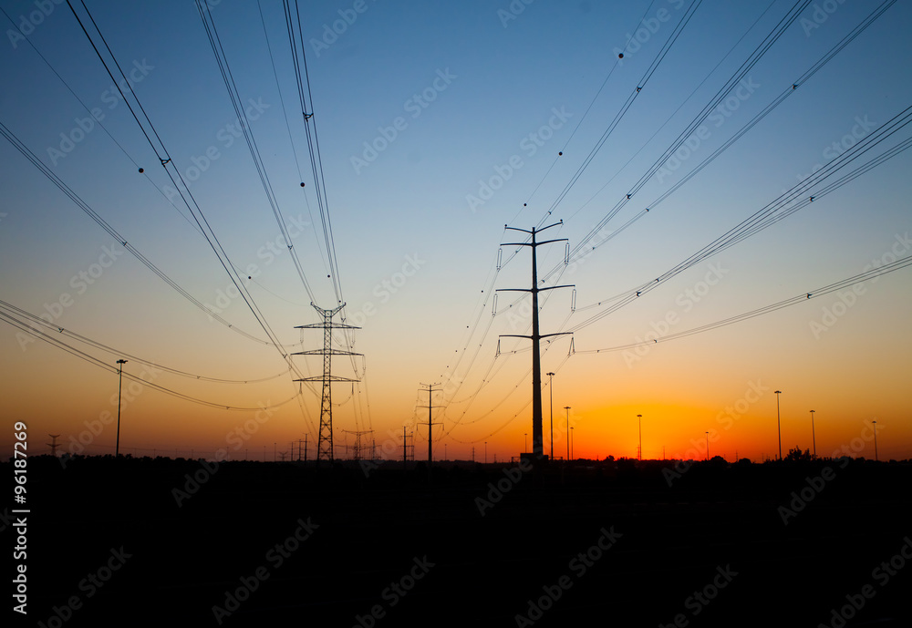 Silhouettes of power transmission line poles at sunset