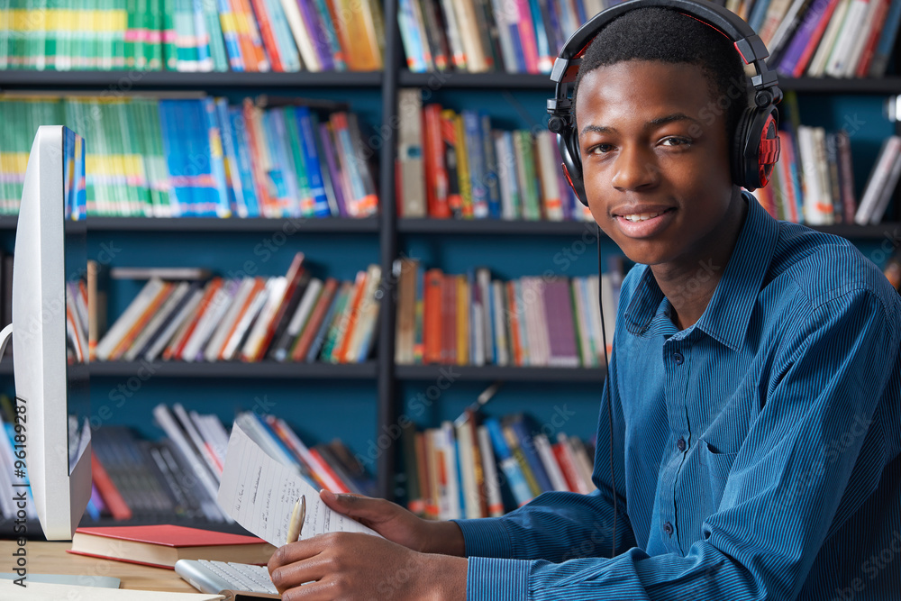 Male Teenage Student Working At Computer Wearing Headphones - obrazy, fototapety, plakaty 