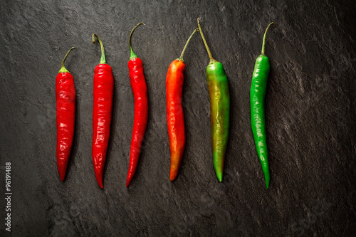 Sechs rote und grüne Peperoni auf Platte aus Naturschiefer