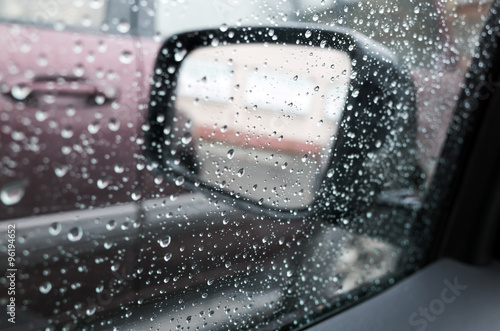 Wet car window with raindrops and a mirror behind