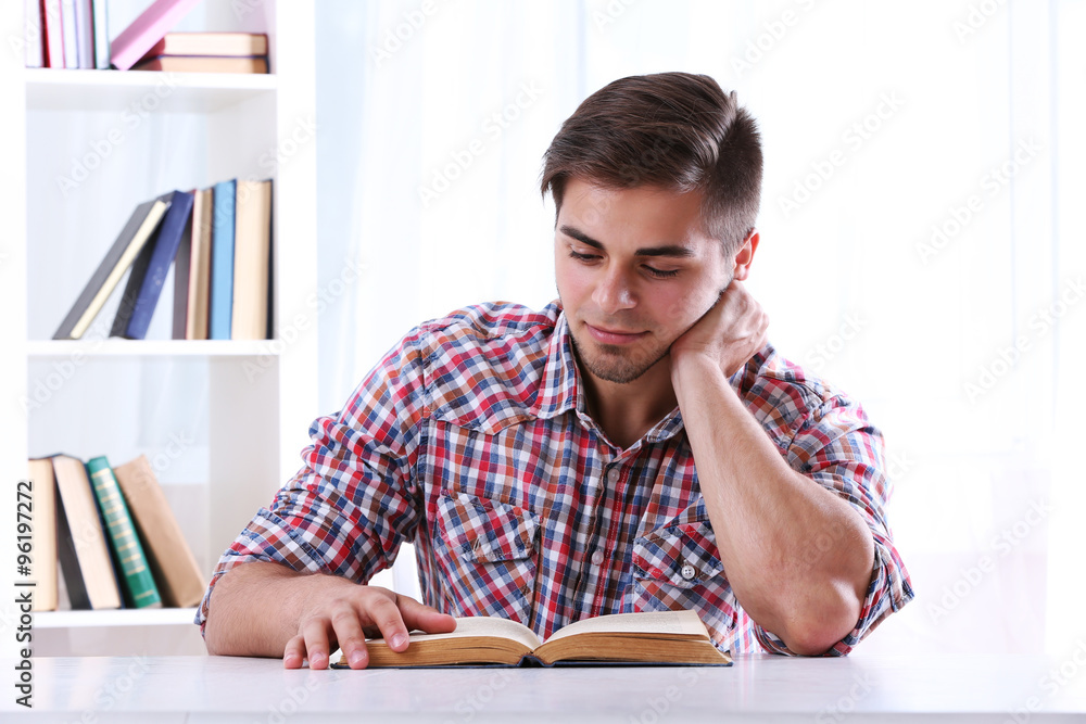Young man reading book at table in room Young man reading book at table in room
