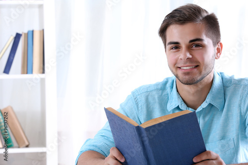 Young man reading book at table in room