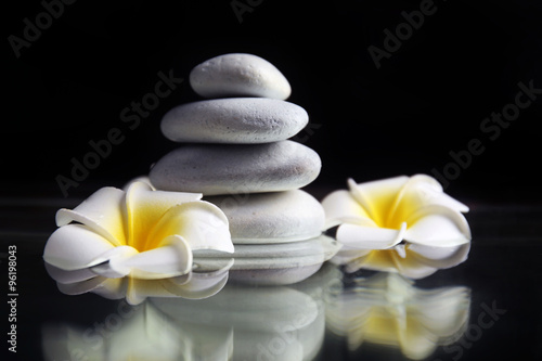 Composition of plumeria flowers and pebbles pile on black background