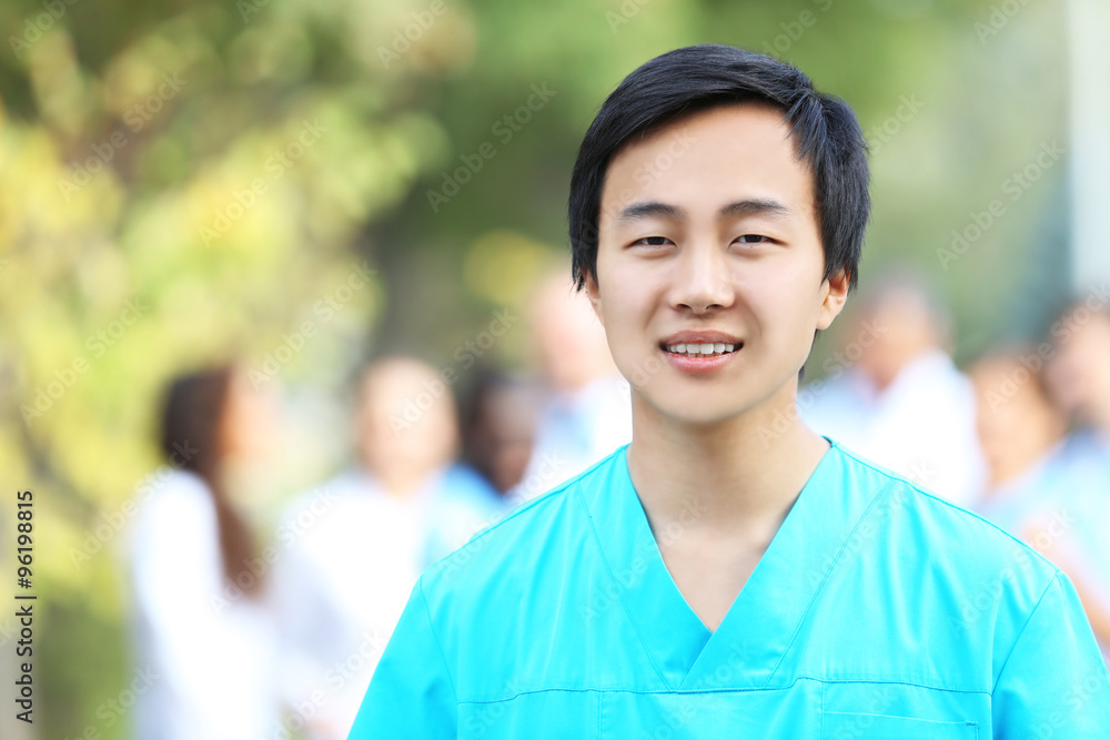 Young smiling doctor standing against unfocused group of medical workers Young smiling doctor standing against unfocused group of medical workers