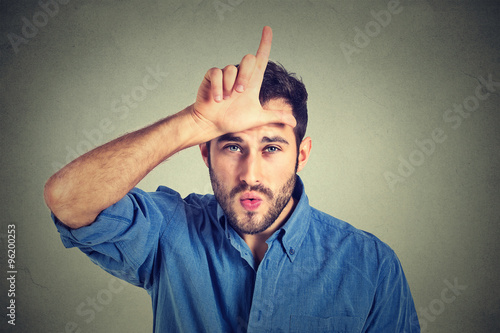 Φωτογραφία young man showing loser sign on forehead, looking at you with disgust