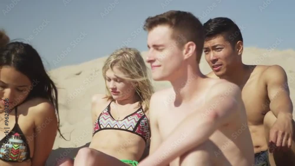 Authentic young group of multi ethnic friends sitting in the sand talking Authentic young group of multi ethnic friends sitting in the sand talking