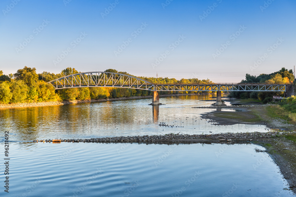 Colorful autumn landscape with the river and railway bridge over dry weather at sunset.