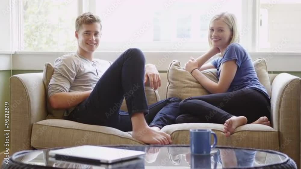 Young couple sitting on couch smiling at camera Young couple sitting on couch smiling at camera