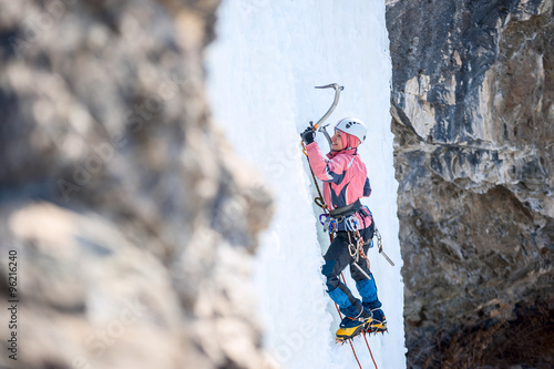 girl mountaineer climbing a frozen waterfall and smiling