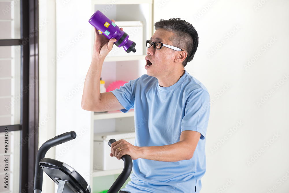 asian senior male drinking water on exercise bike asian senior male drinking water on exercise bike