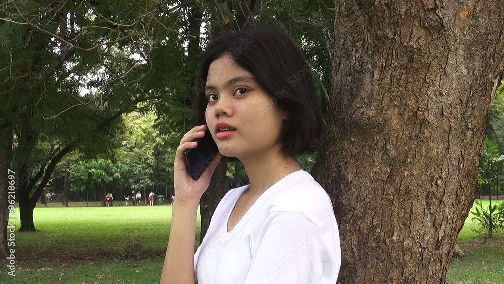 HD Format : Happy young woman talking on mobile phone while sitting under a tree in autumnal park. HD Format : Happy young woman talking on mobile phone while sitting under a tree in autumnal park.