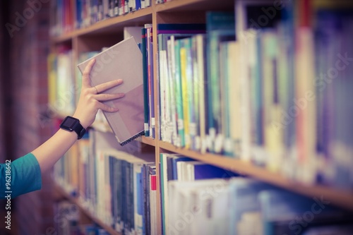 Students hand with smartwatch picking book from bookshelf