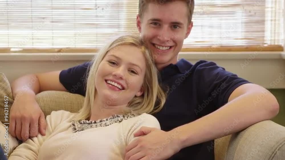 Happy young couple smiling at camera on couch Happy young couple smiling at camera on couch