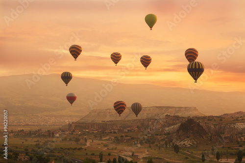 Multi-colored balloons fly over rocks in Cappadocia at sunrise