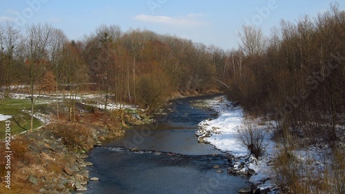 Landscape with river with one bank covered with snow and the other with grass in early spring