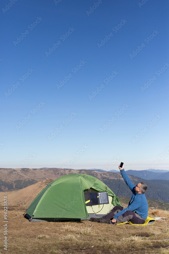 The solar panel attached to the tent. The man sitting next to mobile phone charges from the sun.