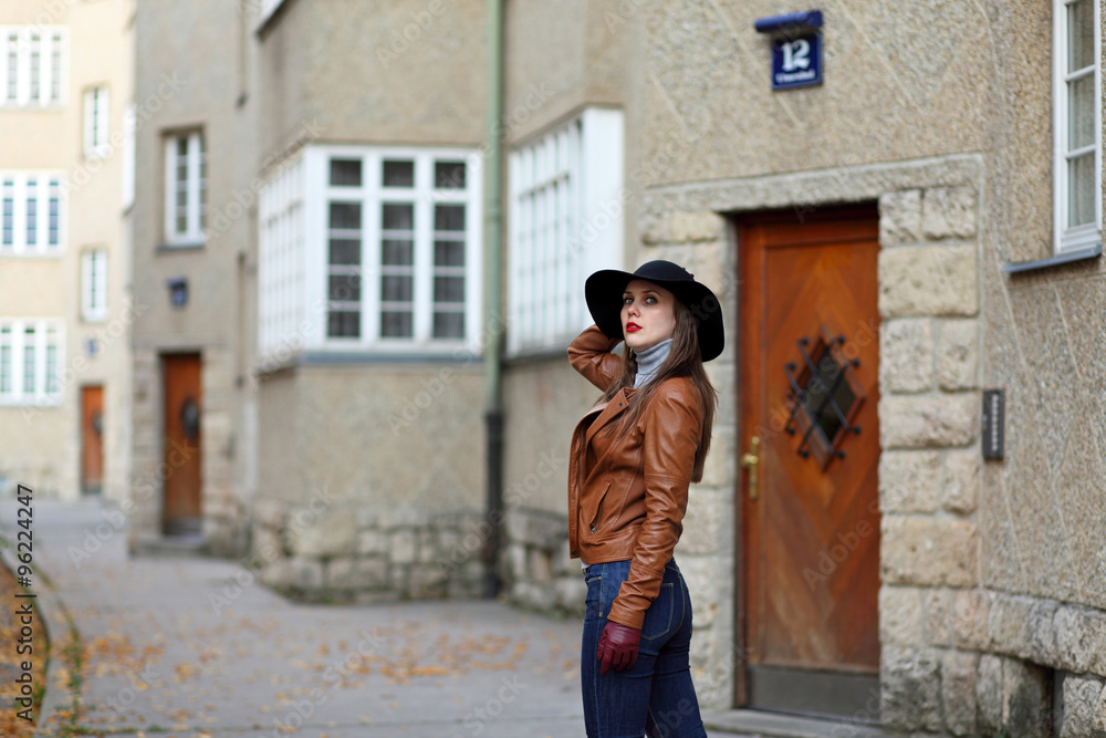 Young woman with hat and leather jacket in front of an appartment building