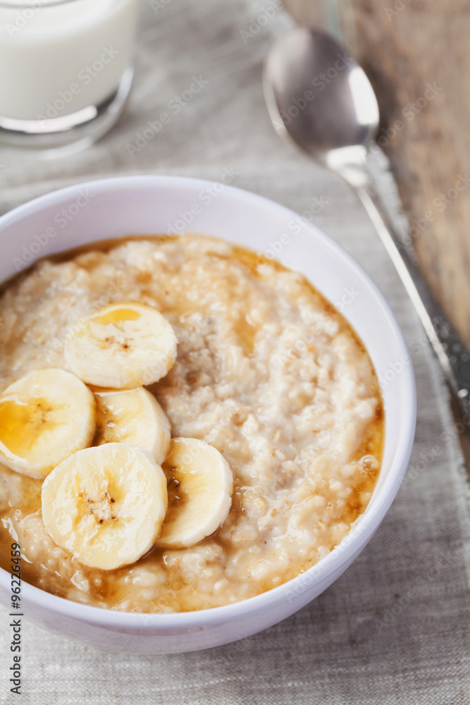 Bowl of oatmeal porridge with banana and caramel sauce on rustic table, hot and healthy breakfast every day, diet food
