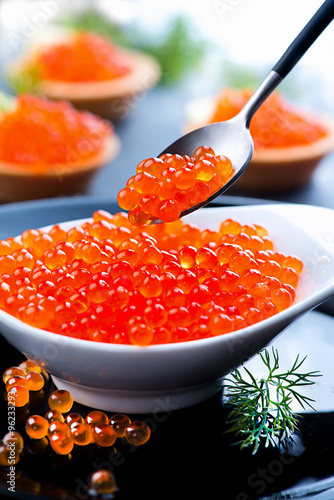 Red caviar. Trout caviar in spoon over black background