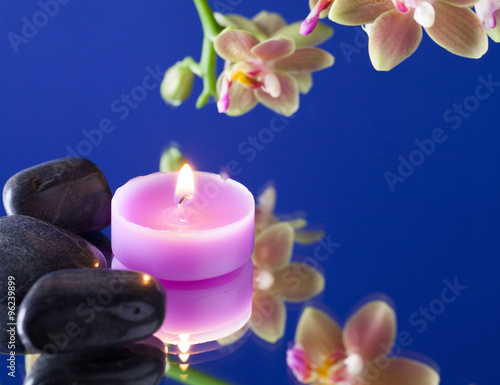 candelina con pietre nere e orchidea su fondo blu