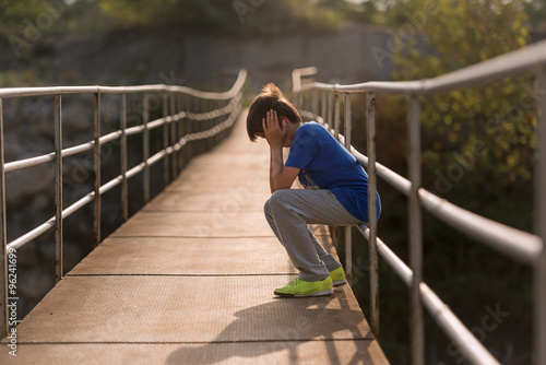 lonely boy sitting on a suspension bridge