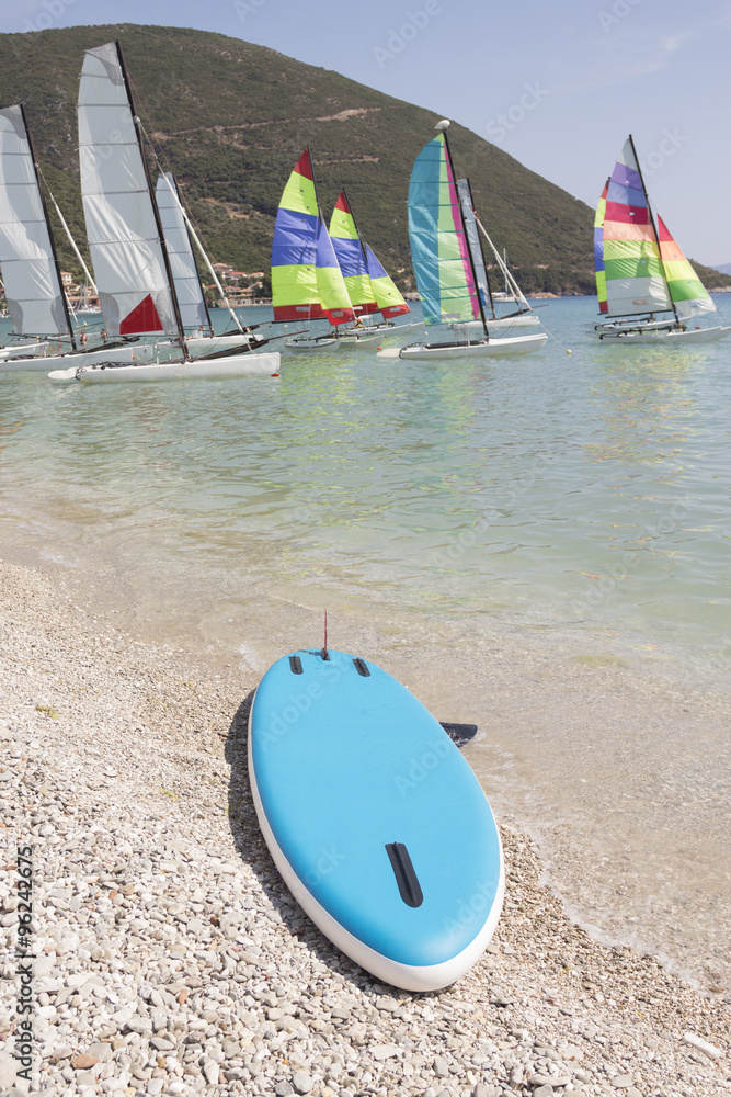 Surfboard on the beach and sailboats in the background