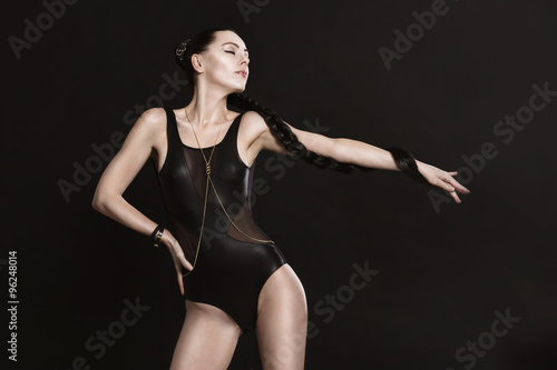Attractive young woman in leather garment is stretched out her left hand. Her long braid wounds of her hand. She's strong, slender, flexible and confident. © lina_aster