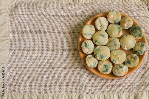 Muffins with salmon, spinach and cheese in big orange plate on center beige linen tablecloth. Aerial view.