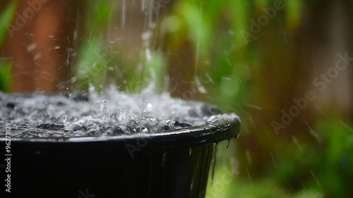 Rain water pouring in black basin with green garden background