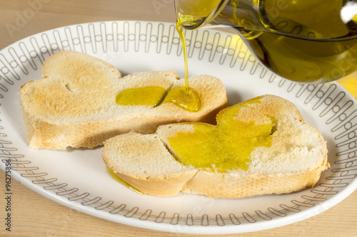 Mediterranean breakfast: pouring Extra Virgin olive oil on a slice of toasted bread.