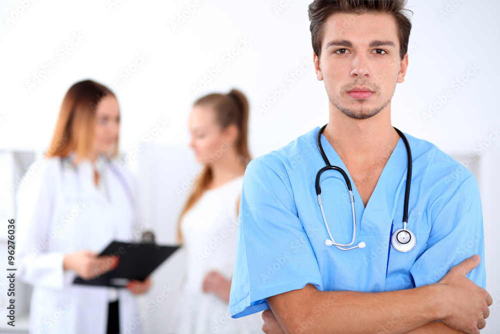 Attractive male doctor in front of medical group, crossed arms Attractive male doctor in front of medical group, crossed arms