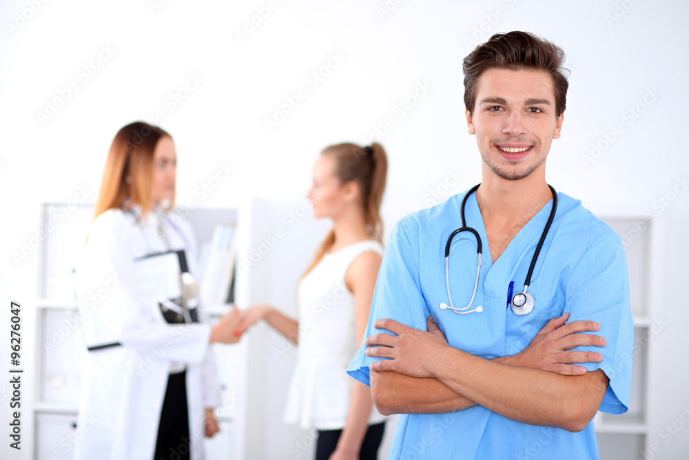Attractive male doctor in front of medical group, crossed arms Attractive male doctor in front of medical group, crossed arms